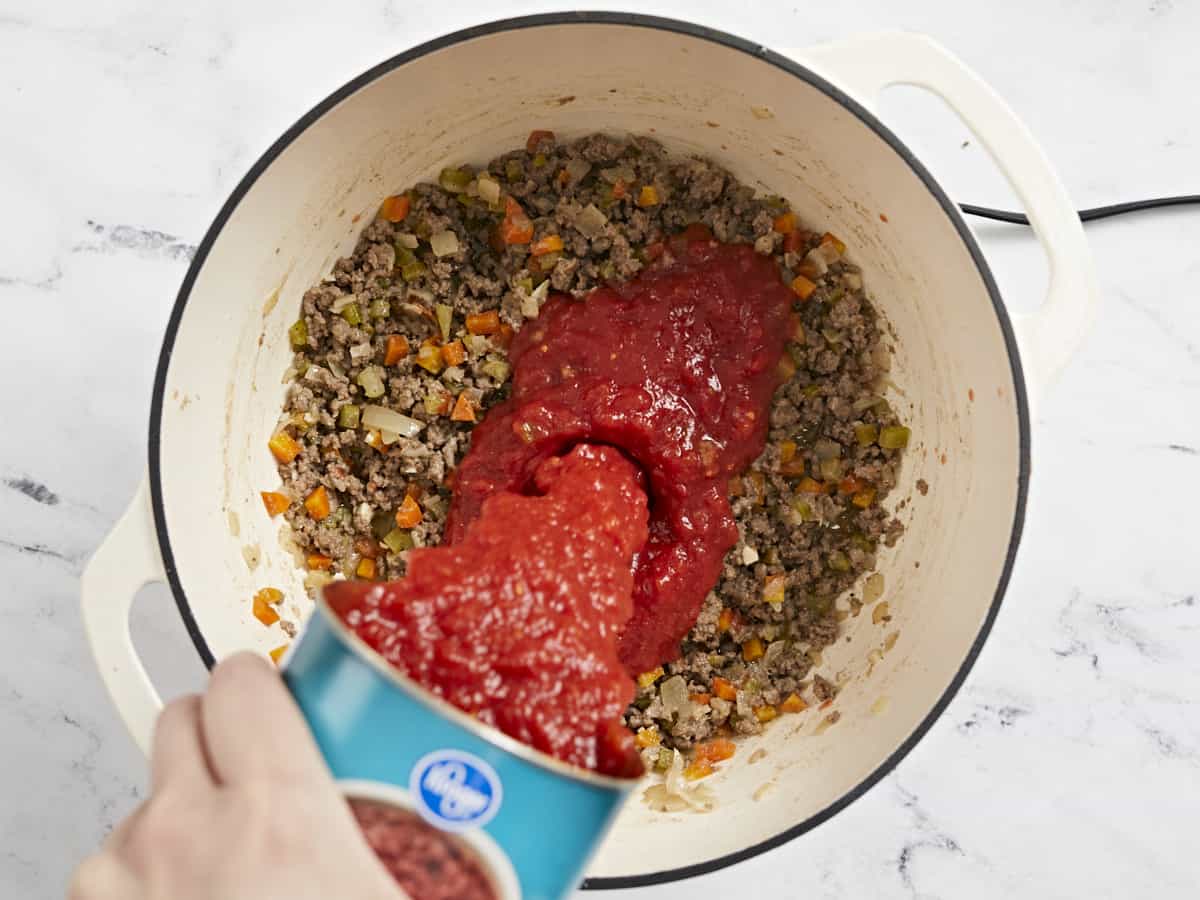 Overhead shot of crushed tomatoes being poured into the browned meat.