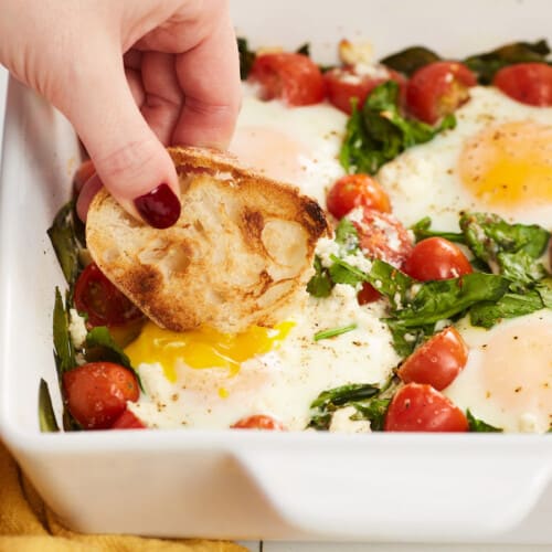 Side view of bread being dipped into a casserole of baked eggs.