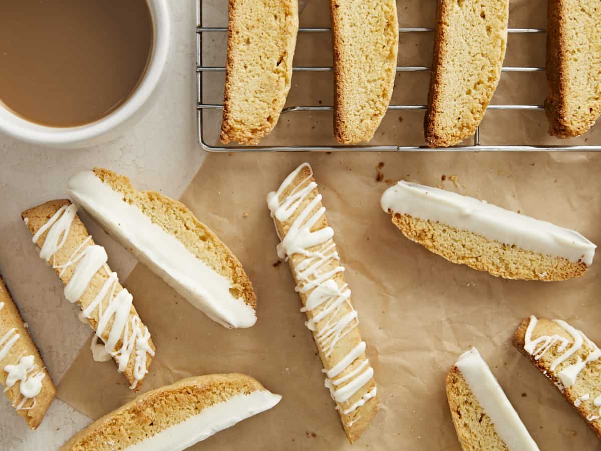 biscotti scattered on a surface with a cooling rack and cup of coffee.