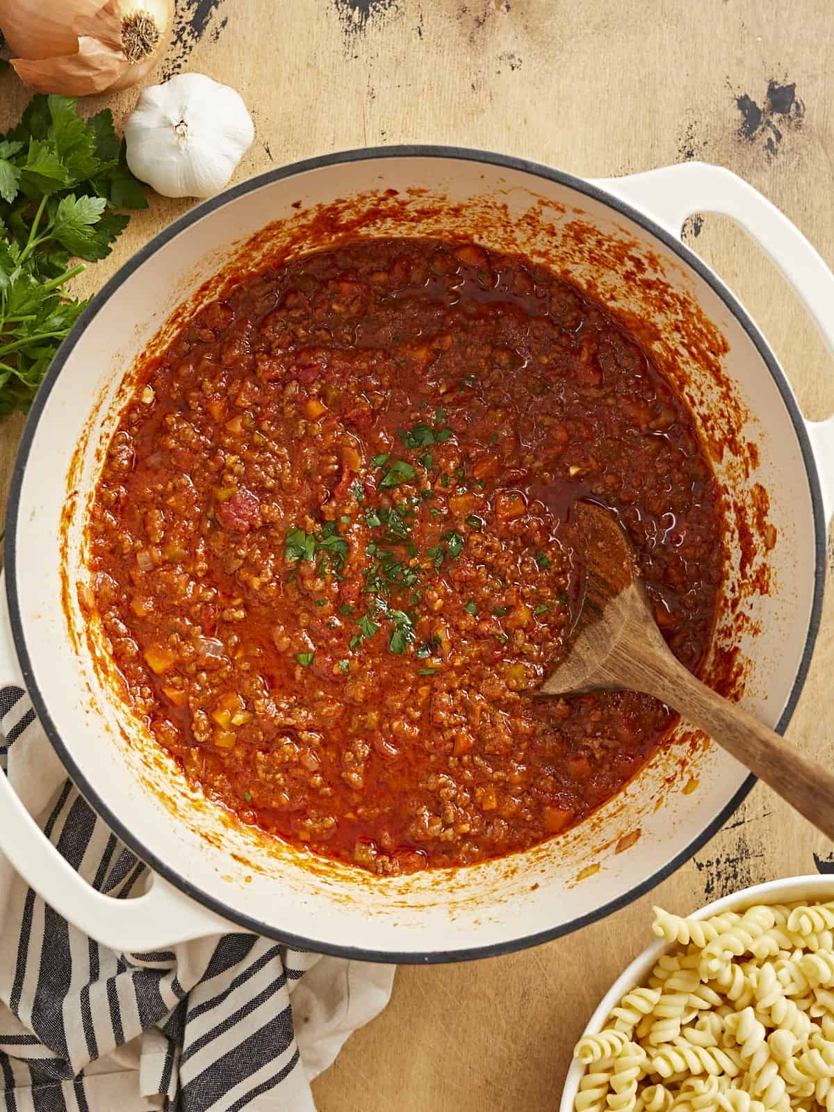 Overhead shot of bolognese in a beige Dutch oven with a wood spoon in it.