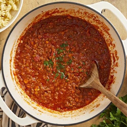 Overhead shot of bolognese in a beige Dutch oven with a wood spoon in it.