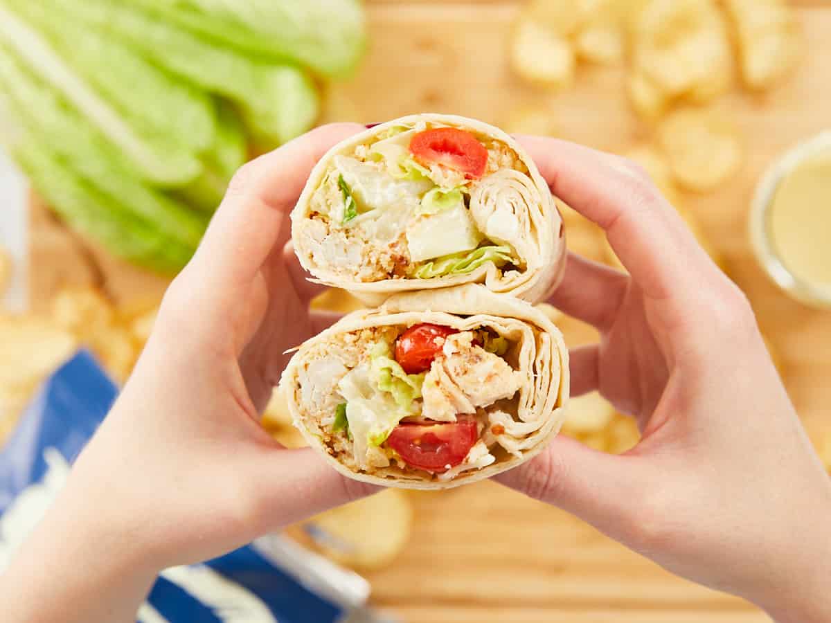 Close up of a hand holding a chicken Caesar wrap cut in half.