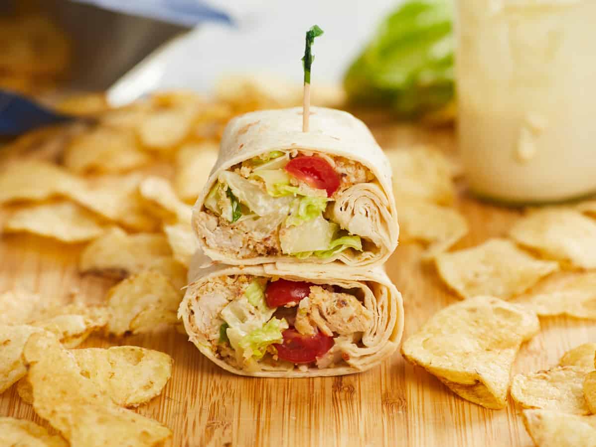 Side view of a chicken Caesar wrap cut in half and stacked on a cutting board.