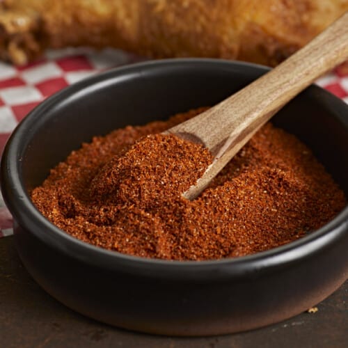 Side shot of Nashville Hot Seasoning Blend in a black bowl with a wood spoon in it.