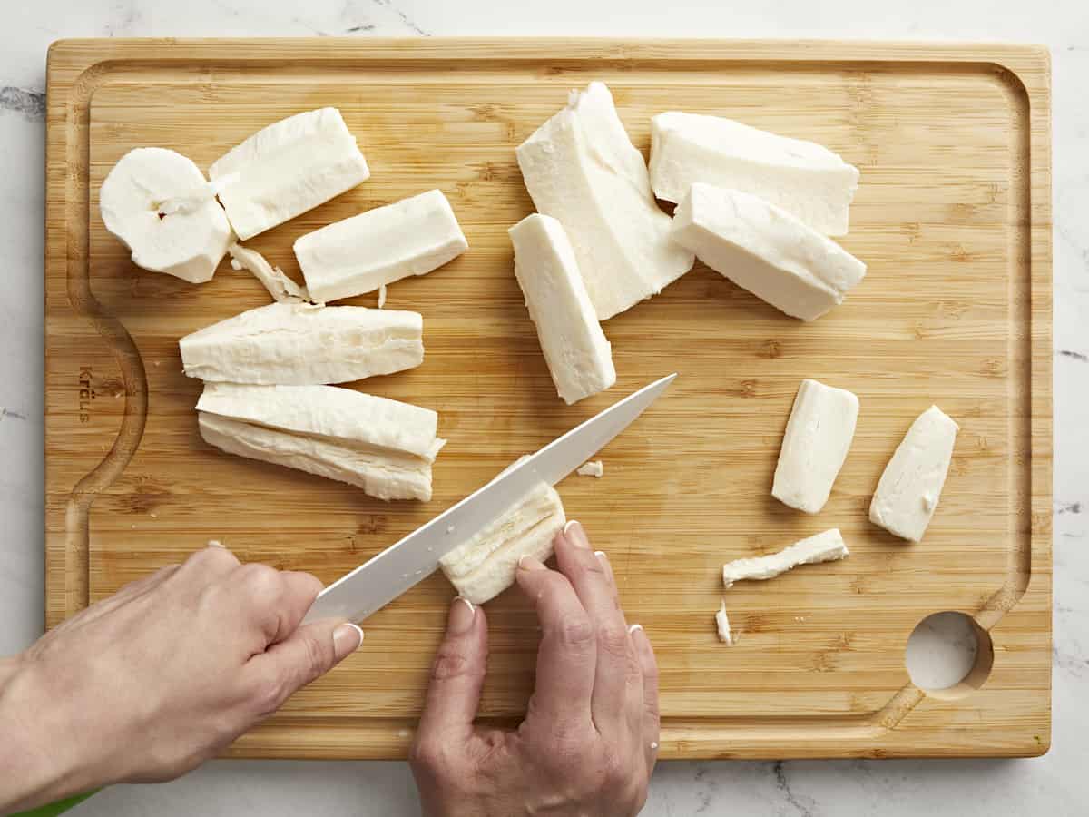 Overhead shot of yuca on a cutting board with a knife removing the woody core.