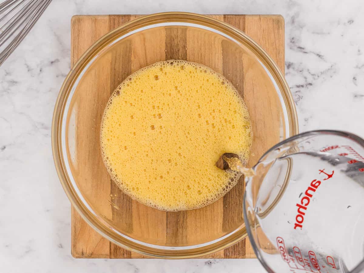 Water being added to whisked eggs in a bowl.