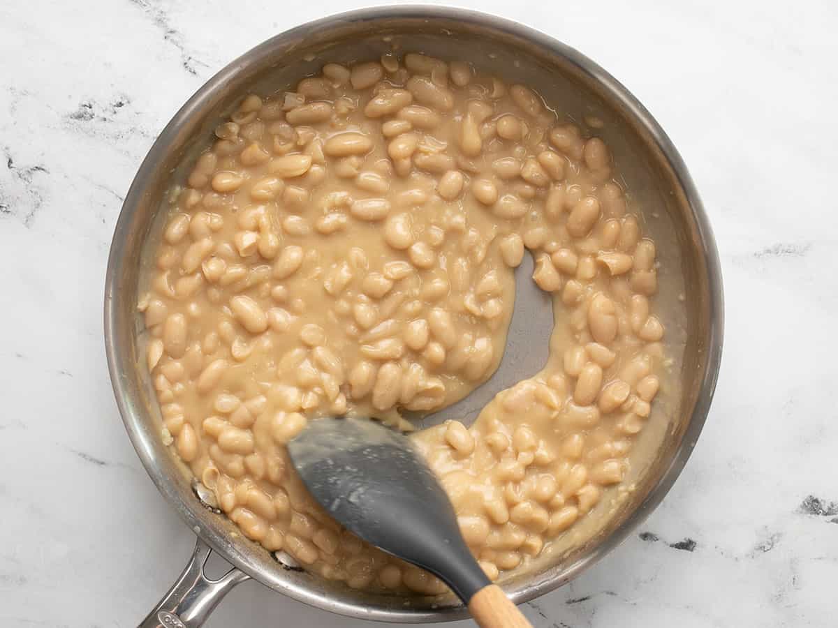 Simmered beans in the skillet being stirred with a spoon.