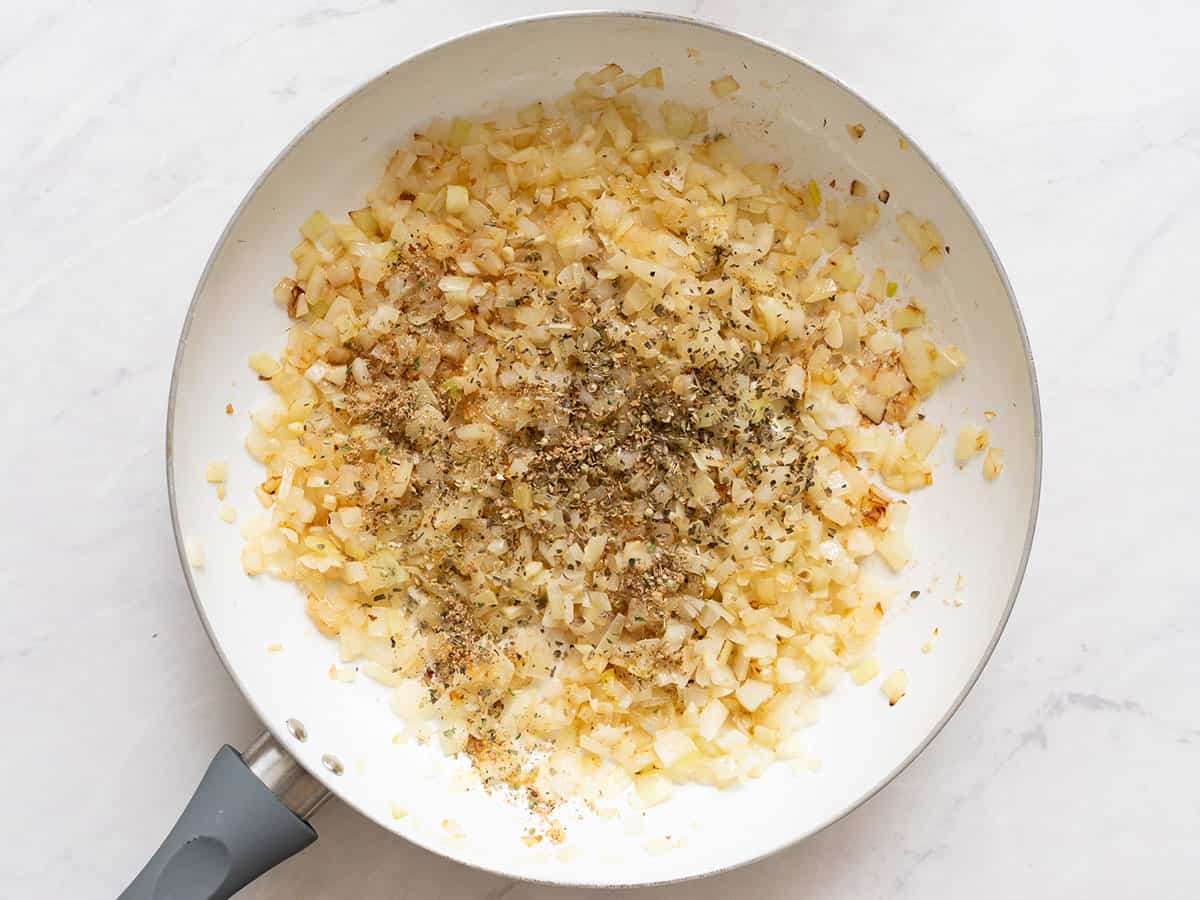 Overhead view of sauteed onions, garlic and Italian seasoning in a large skillet.