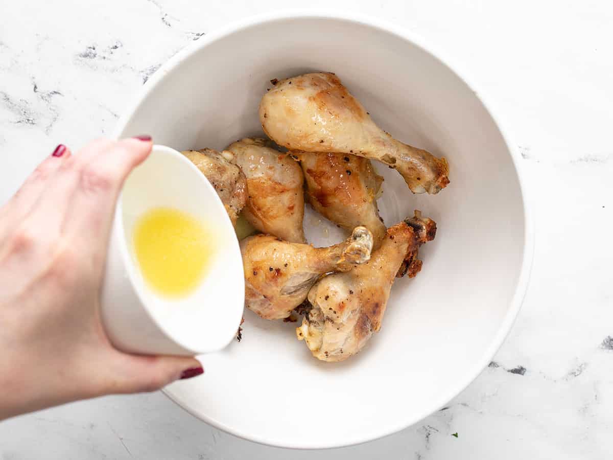 Melted butter being drizzled over the drumsticks in a bowl.