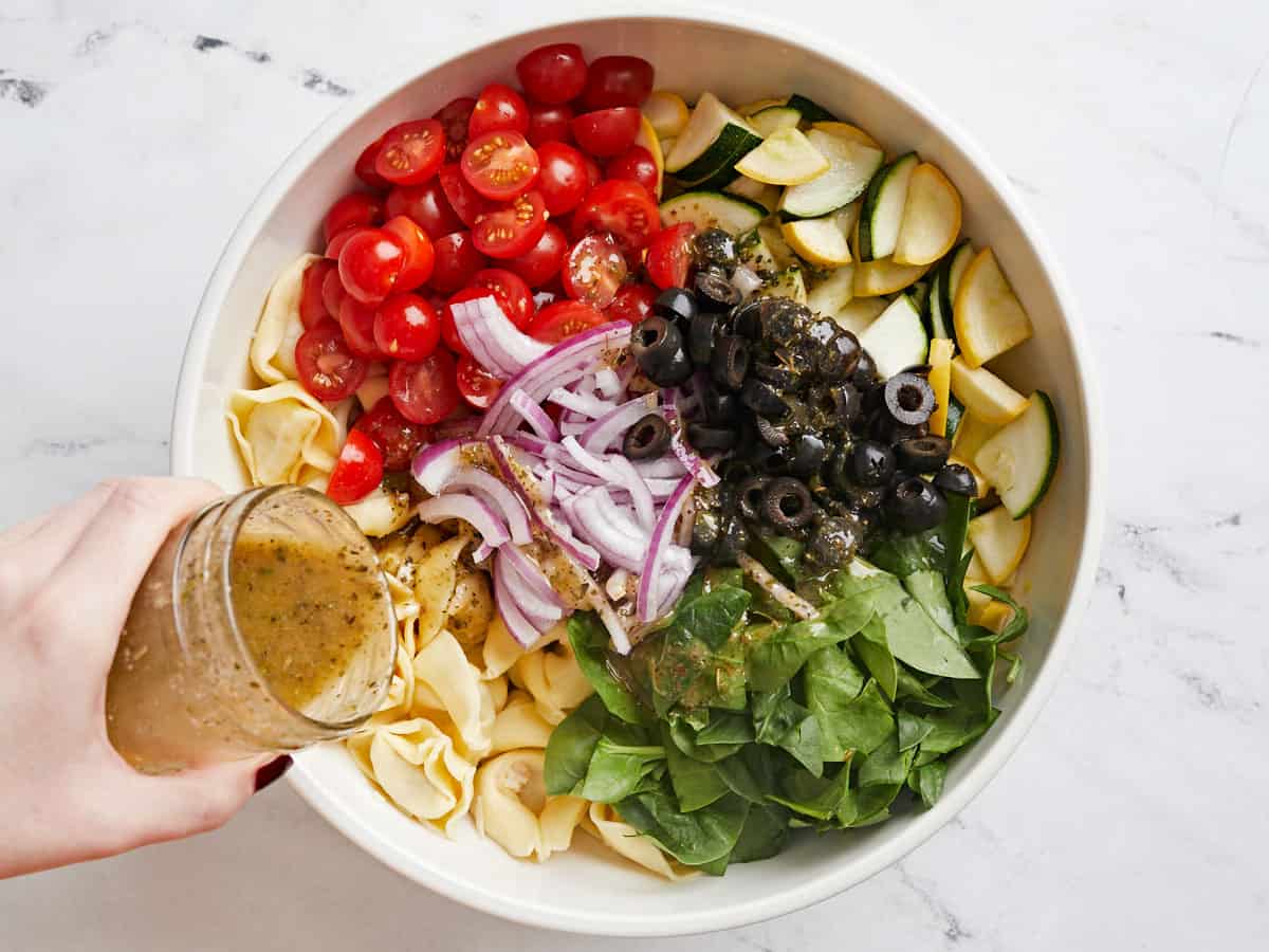 Tortellini salad ingredients in a bowl with Italian dressing being drizzled over top. 