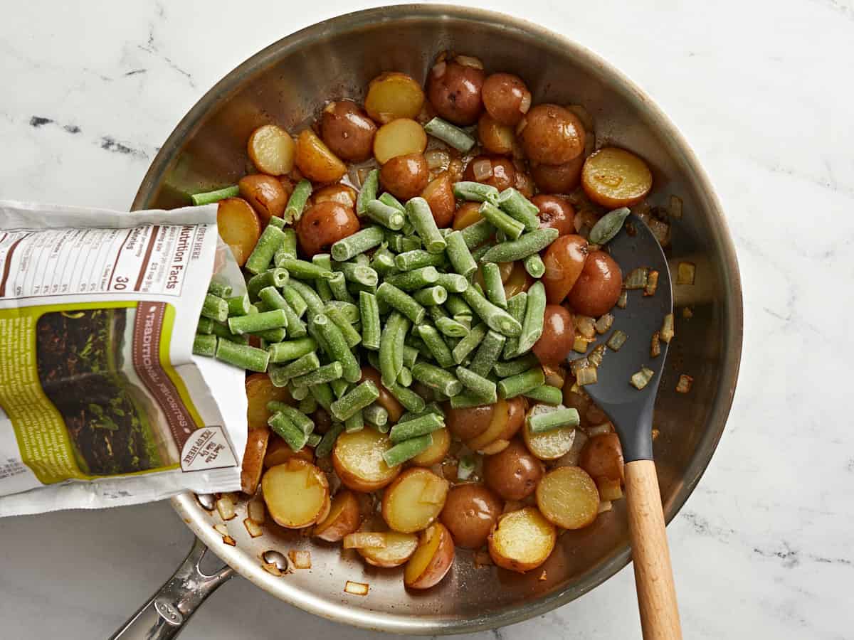 Frozen green beans being poured into the skillet.