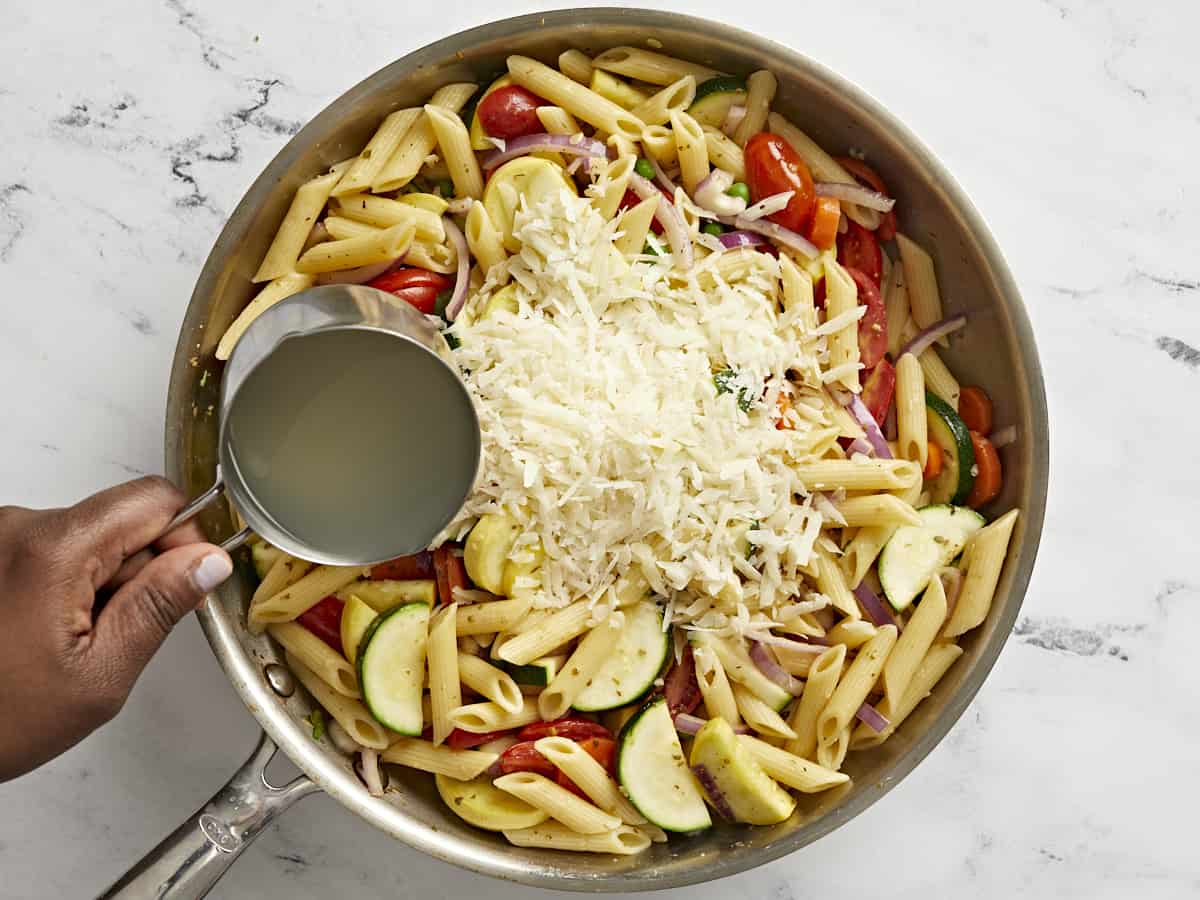 Parmesan added to the skillet and pasta water being drizzled over top.