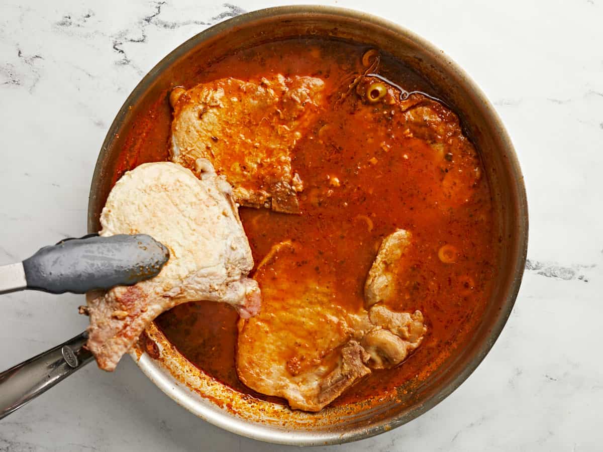 Pork chops being added back to the sauce in the skillet. 