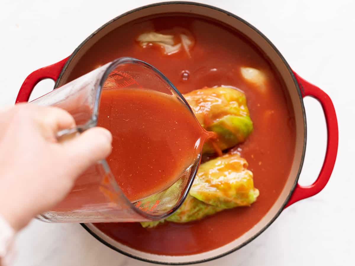 Overhead view of tomato sauce mixture being poured over cabbage leaves inside dutch oven.