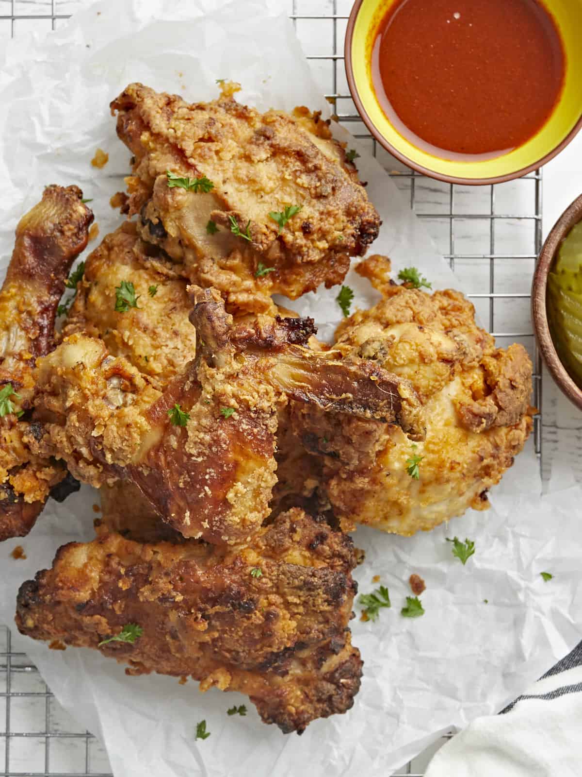 Overhead view of Air Fryer Fried Chicken resting on parchment paper and a cooling rack with a small bowl of hot sauce in the background.