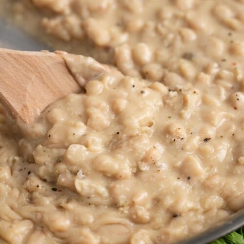 Close up side view of a wooden spoon stirring Parmesan Beans.