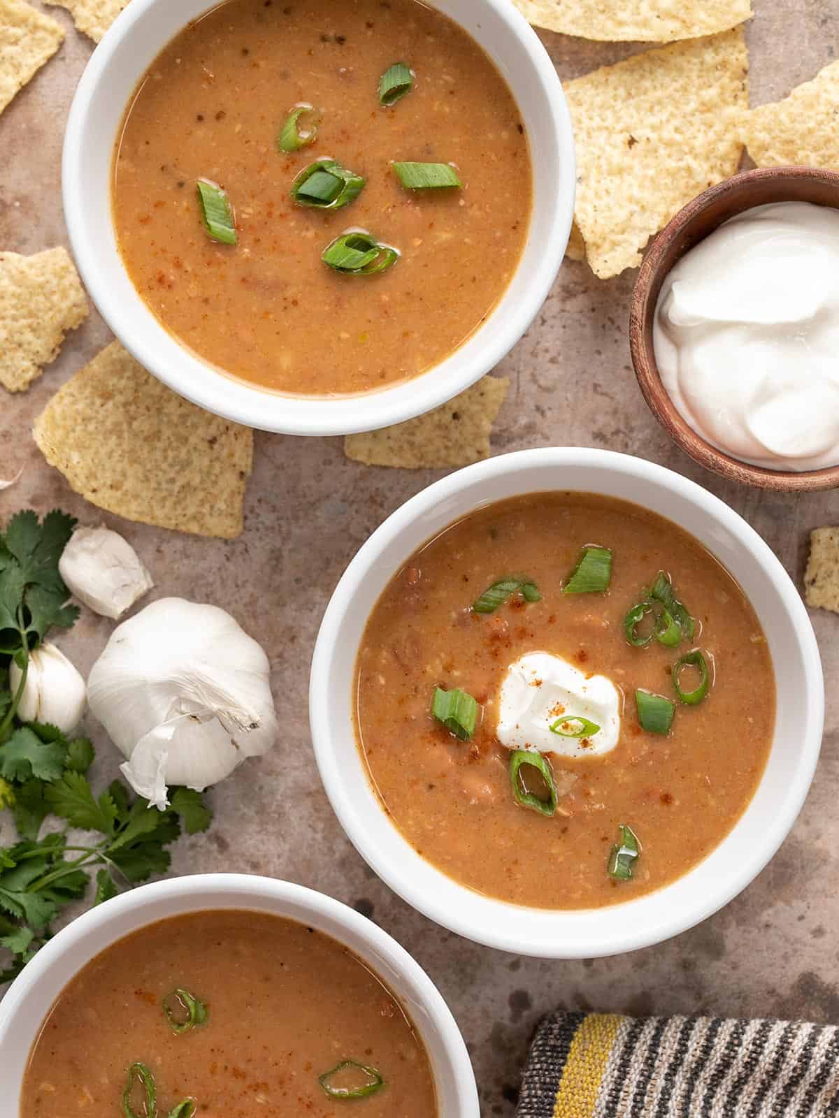 Three bowls of pinto bean soup with toppings all around.