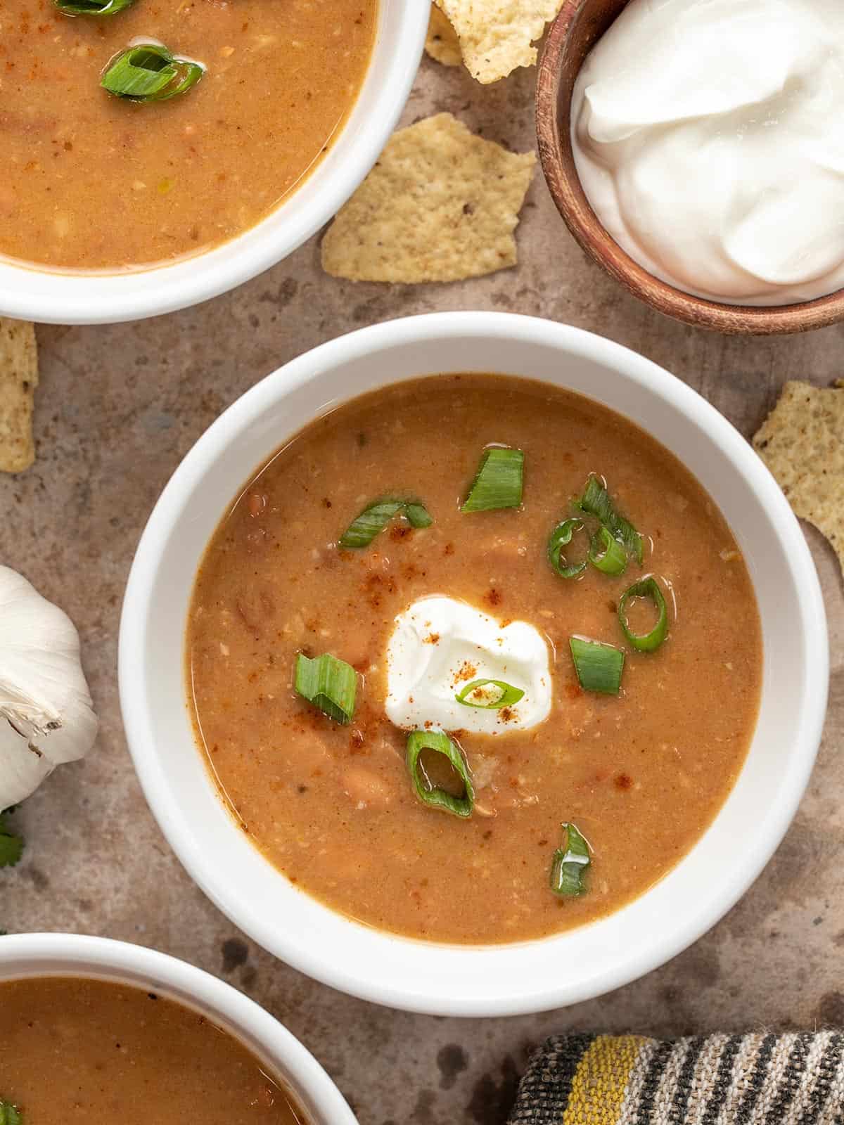 Close up overhead view of three bowls of pinto bean soup with sour cream and green onions.