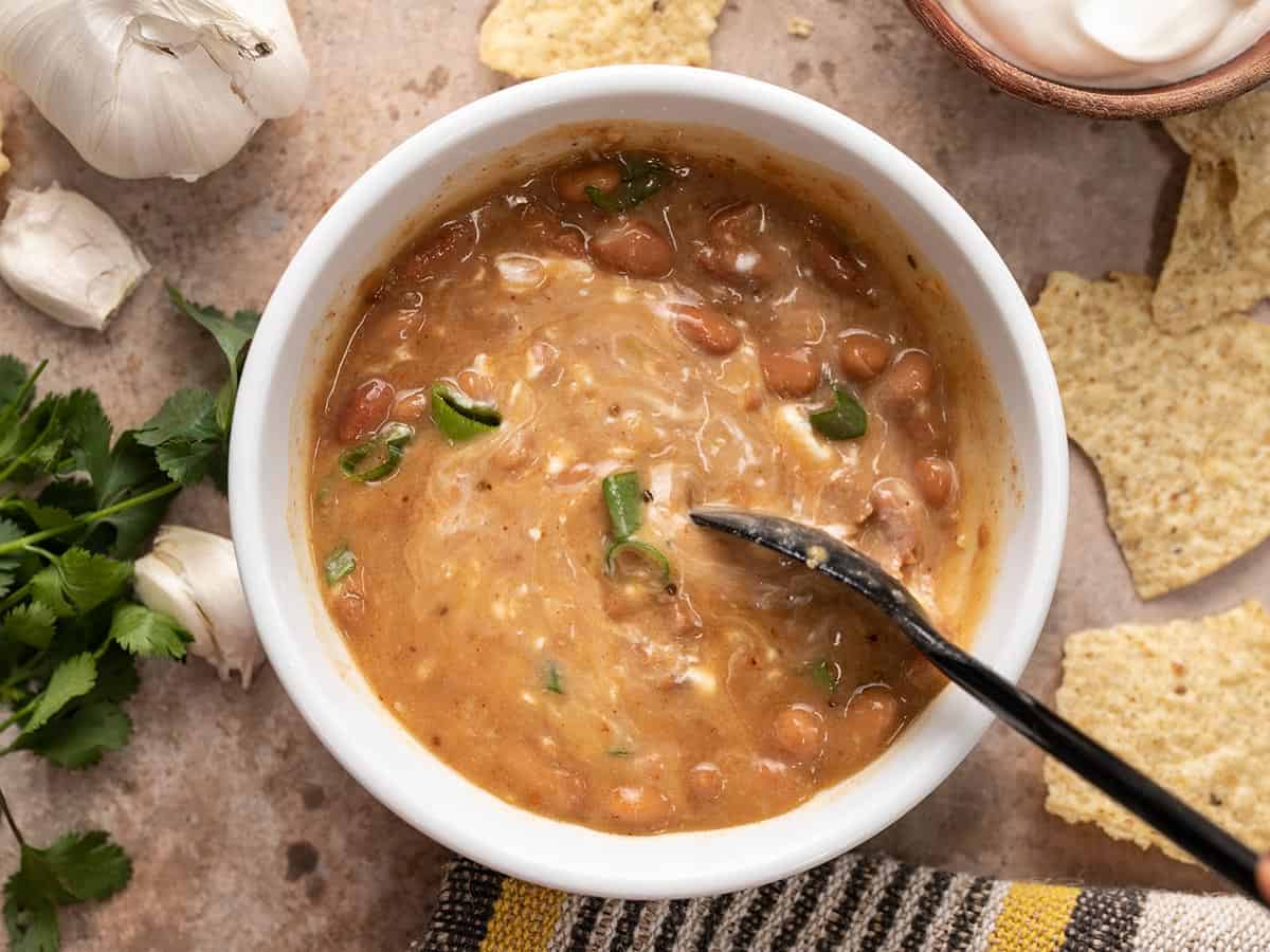 Sour cream being stirred into a bowl of pinto bean soup.