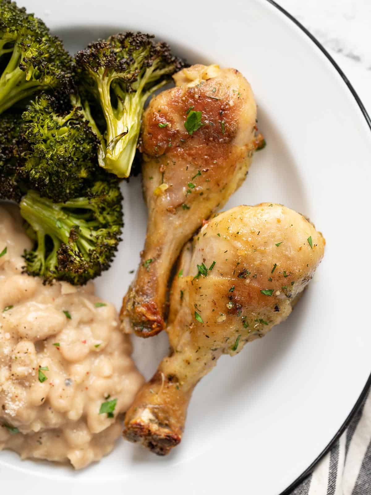 Overhead view of two ranch chicken drumsticks on a plate with beans and broccoli.