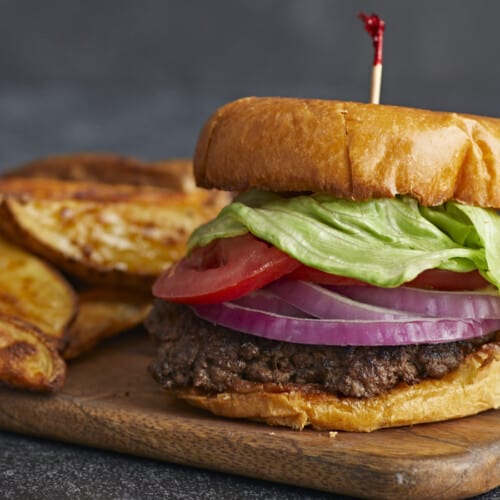 Side shot of a Smash Burger with a toothpick in the bun and french fries in the background.