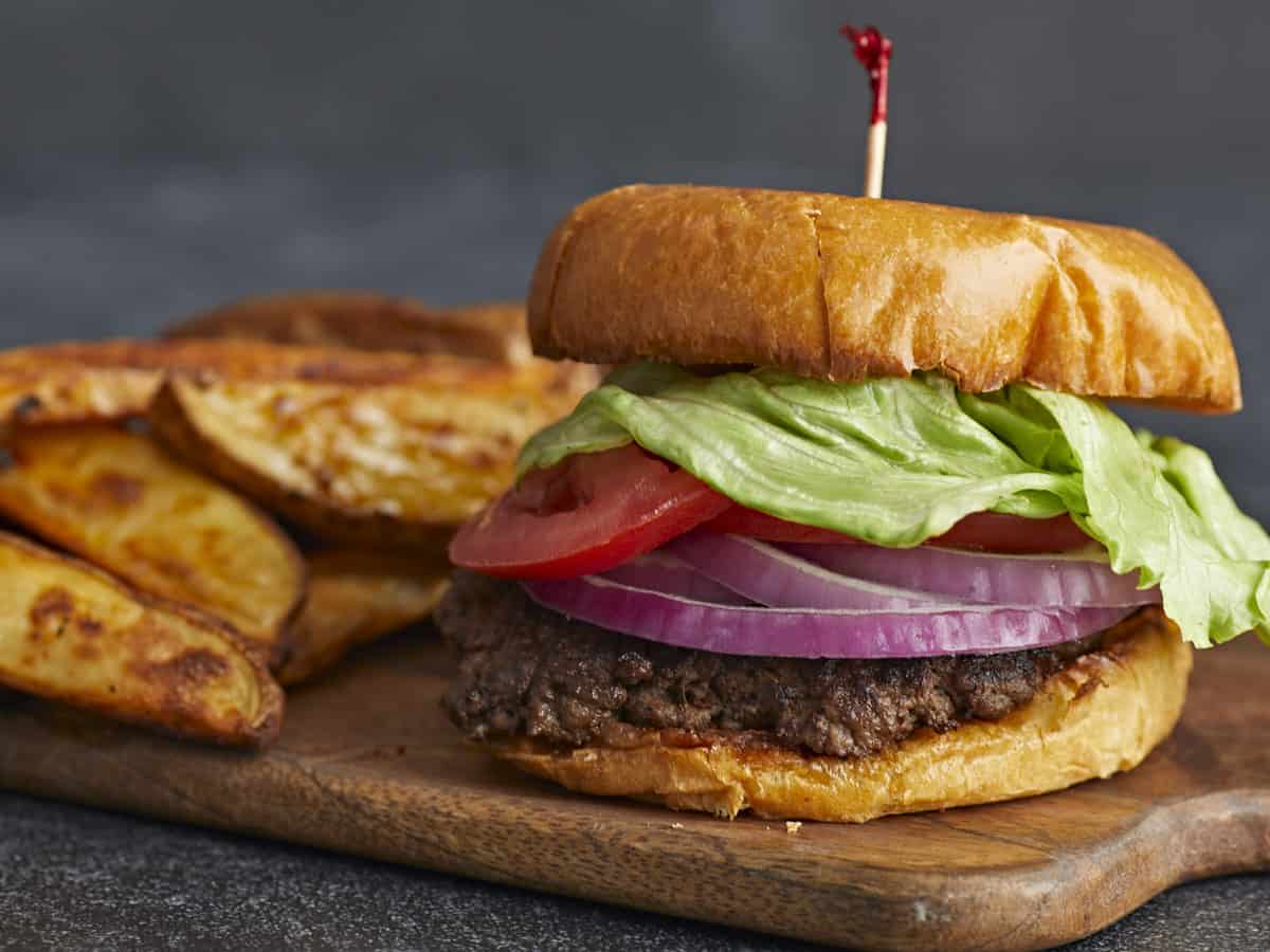 Side shot of a Smash Burger with a toothpick in the bun and french fries in the background.