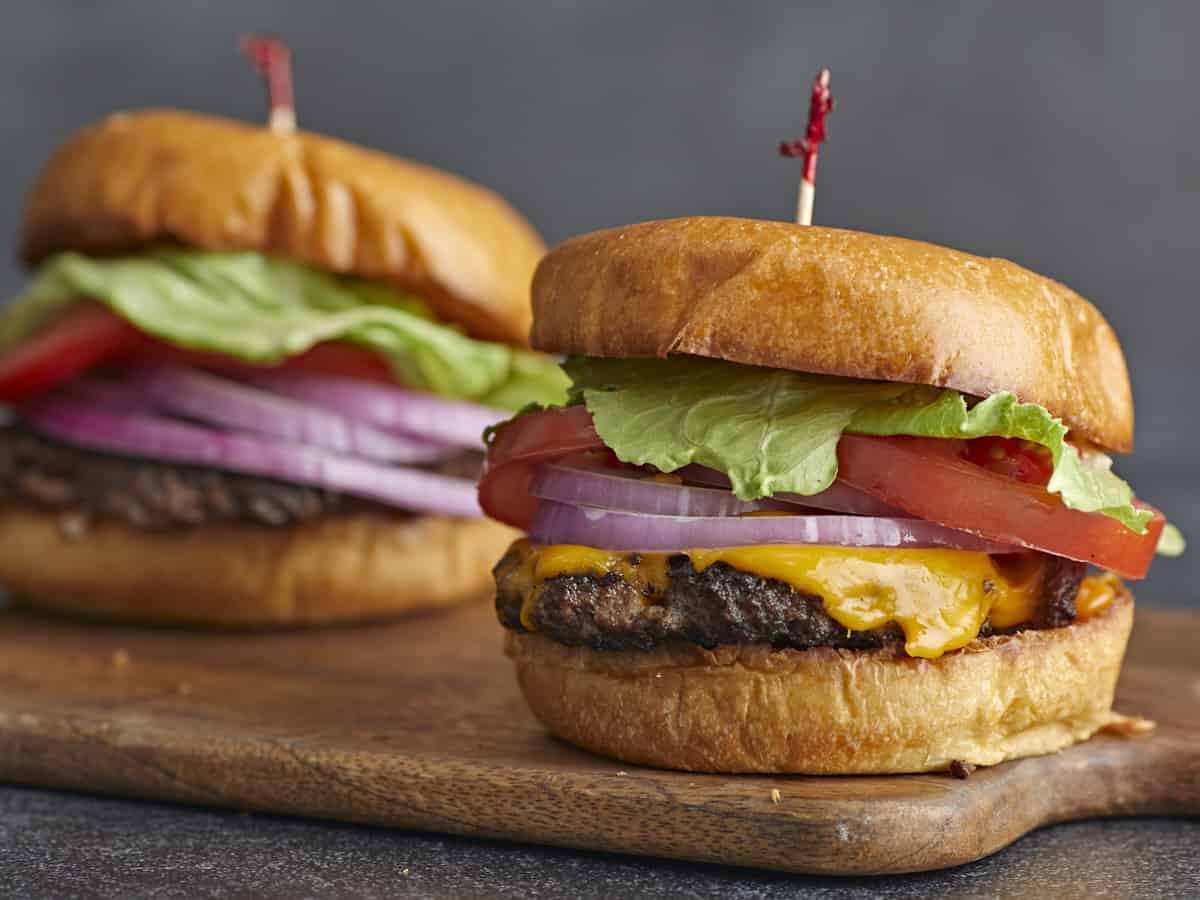 Side shot of a Smash Burger with a toothpick in the bun with a second Smash Burger in the background.