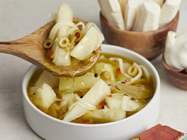 Side shot of Yuca En Escabeche in a white bowl with a wood spoon in it.