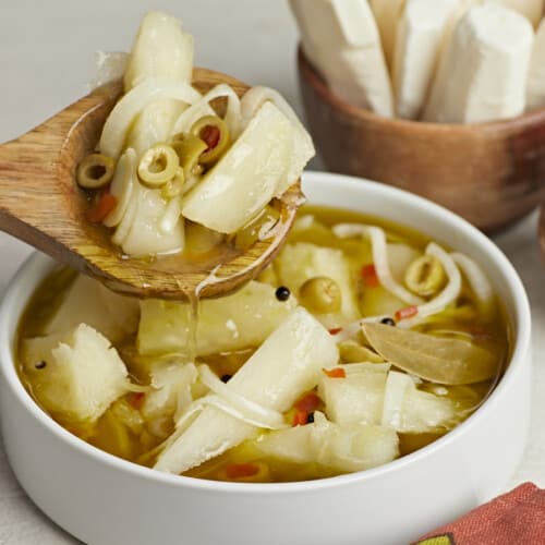 Side shot of Yuca En Escabeche in a white bowl with a wood spoon in it.