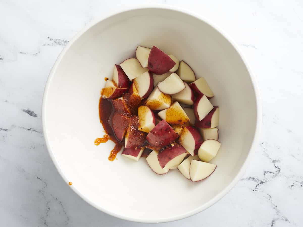 Overhead shot of potatoes being dressed in a white bowl.