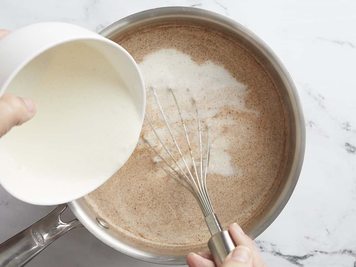 Overhead shot of cornstarch slurry being whisked into a silver pot.