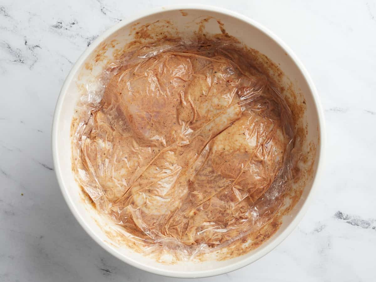 Overhead shot of chicken in a white bowl covered in buttermilk brine.