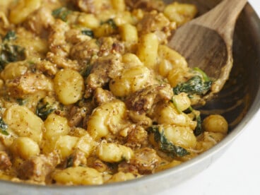 Side shot of Creamy Chicken and Gnocchi in a silver skillet with a wooden spoon in it.