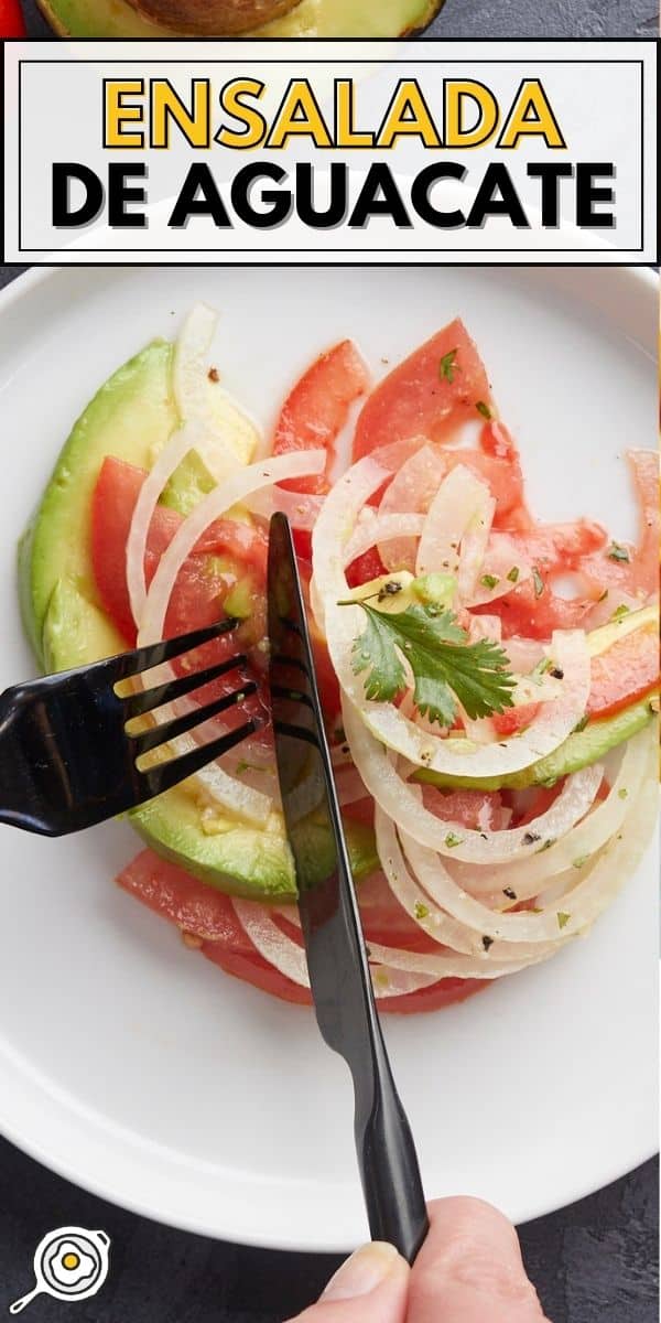 Overhead shot of Ensalada de Aguacate on a white plate with a black fork and knife cutting into it.