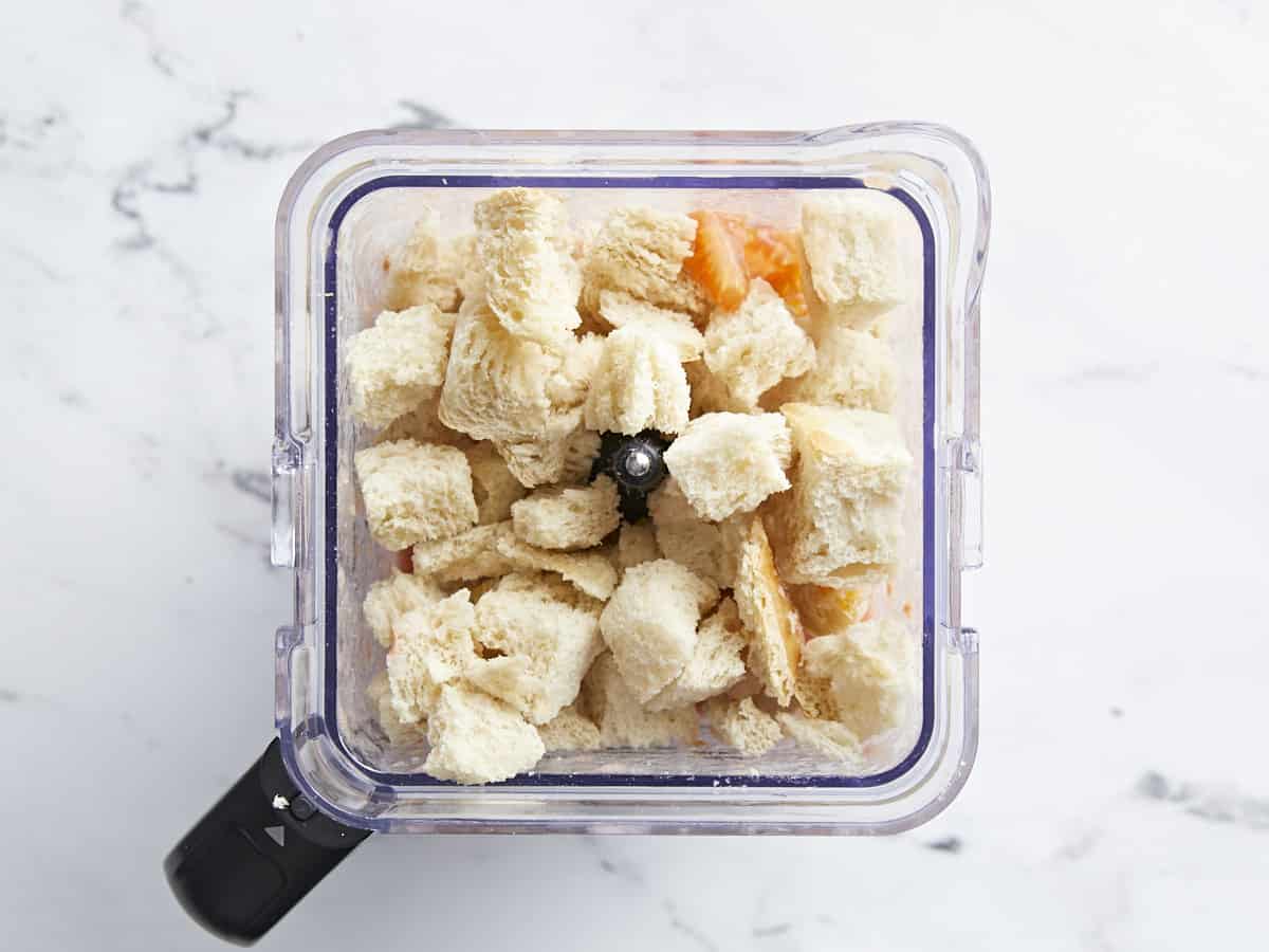 Overhead shot of Salmorejo ingredients topped with cubed bread in a blender jar.