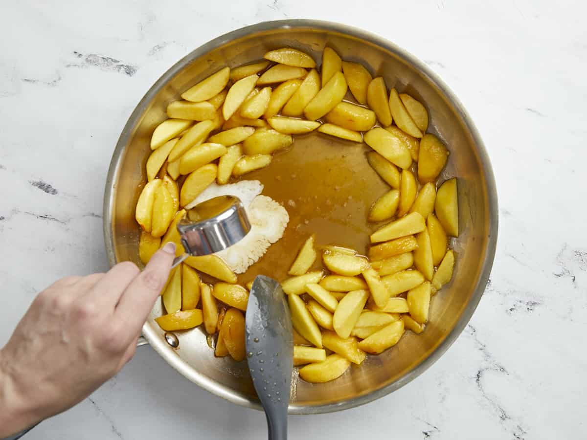 Overhead shot of of cornstarch slurry being added to peaches in a silver pan.