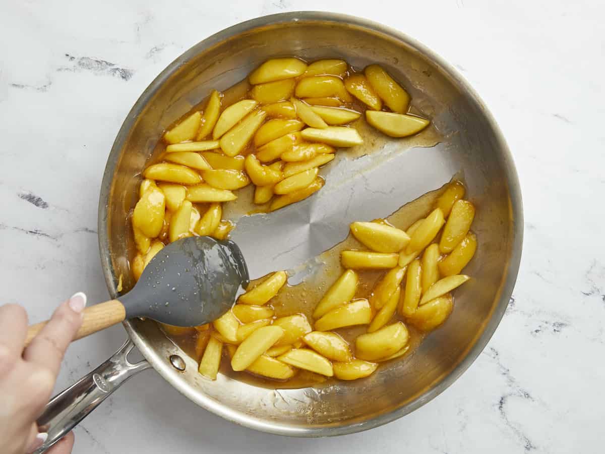 Overhead shot of of peaches being cooked in a silver pan to thicken their juices.