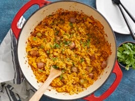 Overhead shot of wooden spoon in a red Dutch oven full of Arroz Con Salchichas.