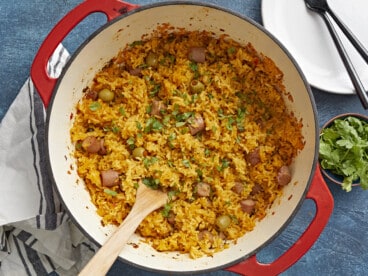 Overhead shot of wooden spoon in a red Dutch oven full of Arroz Con Salchichas.