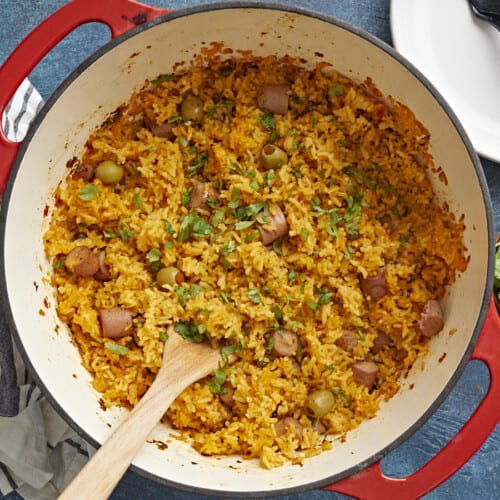 Overhead shot of wooden spoon in a red Dutch oven full of Arroz Con Salchichas.