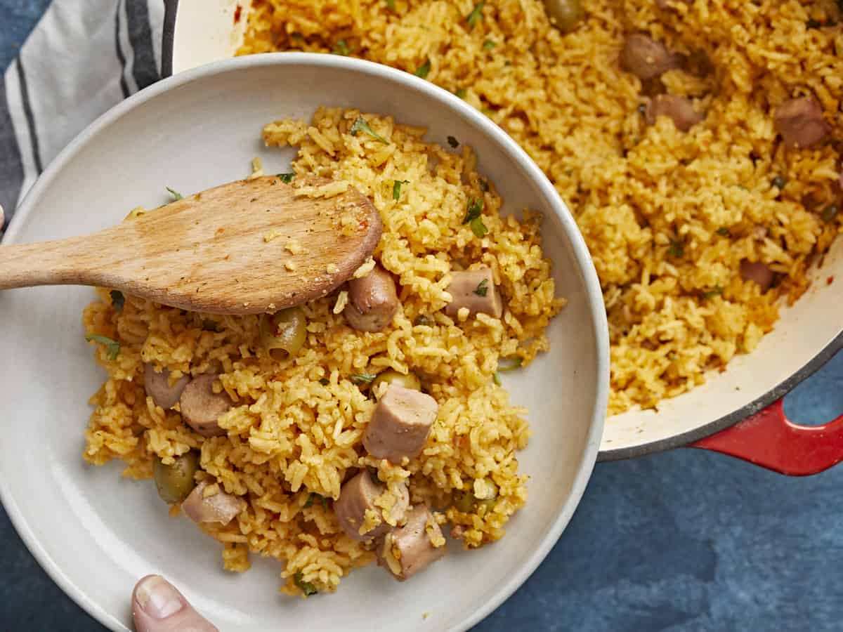 Overhead shot of wooden spoon serving rice out of a red Dutch oven onto a white plate.