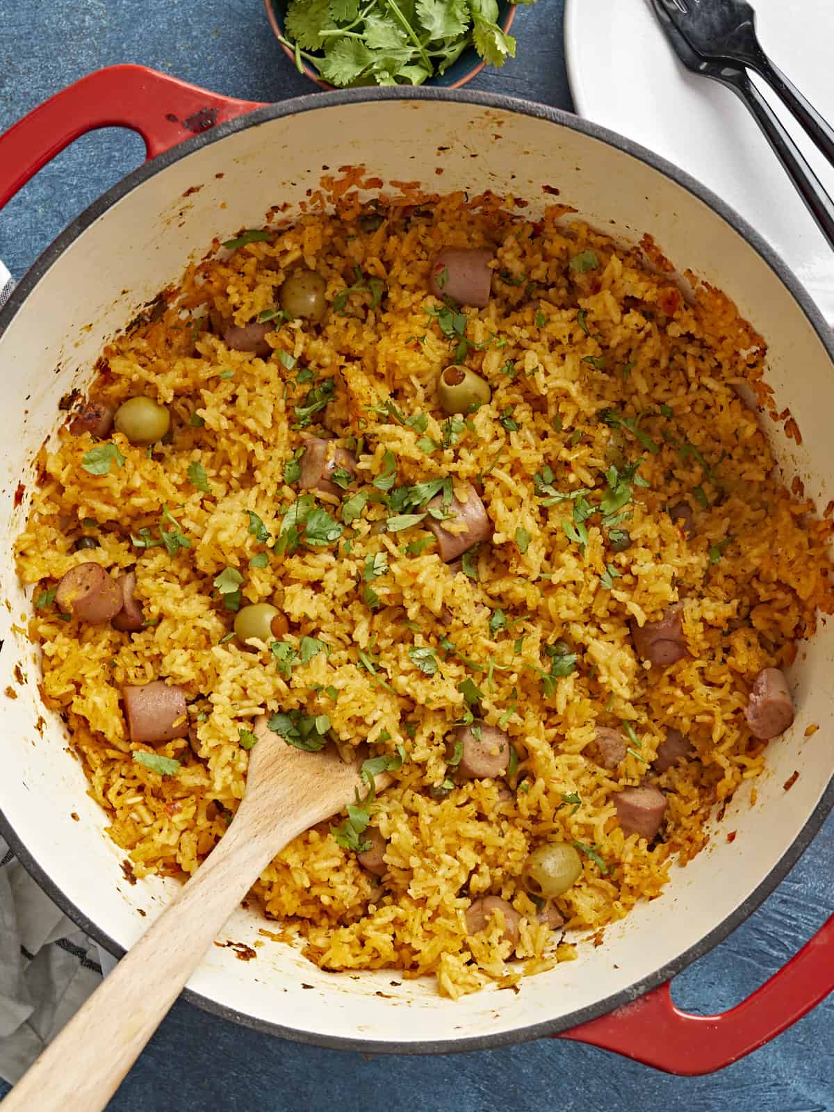 Overhead shot of wooden spoon in a red Dutch oven full of Arroz Con Salchichas.