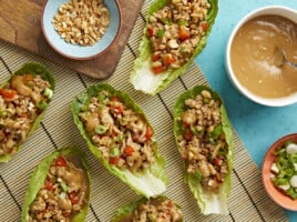 Overhead shot of chicken lettuce wraps with bowls of chopped peanuts, chopped green onions and peanut lime dressing on the side.