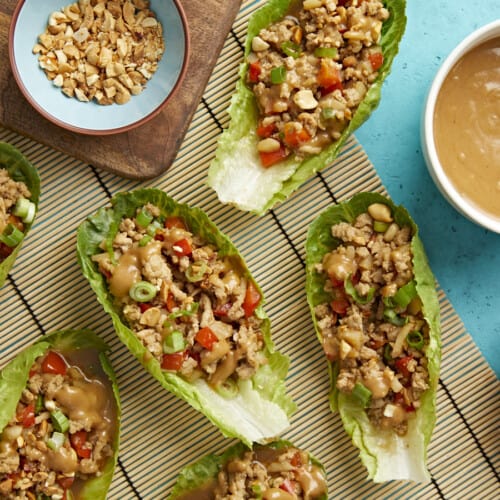 Overhead shot of chicken lettuce wraps with bowls of chopped peanuts, chopped green onions and peanut lime dressing on the side.