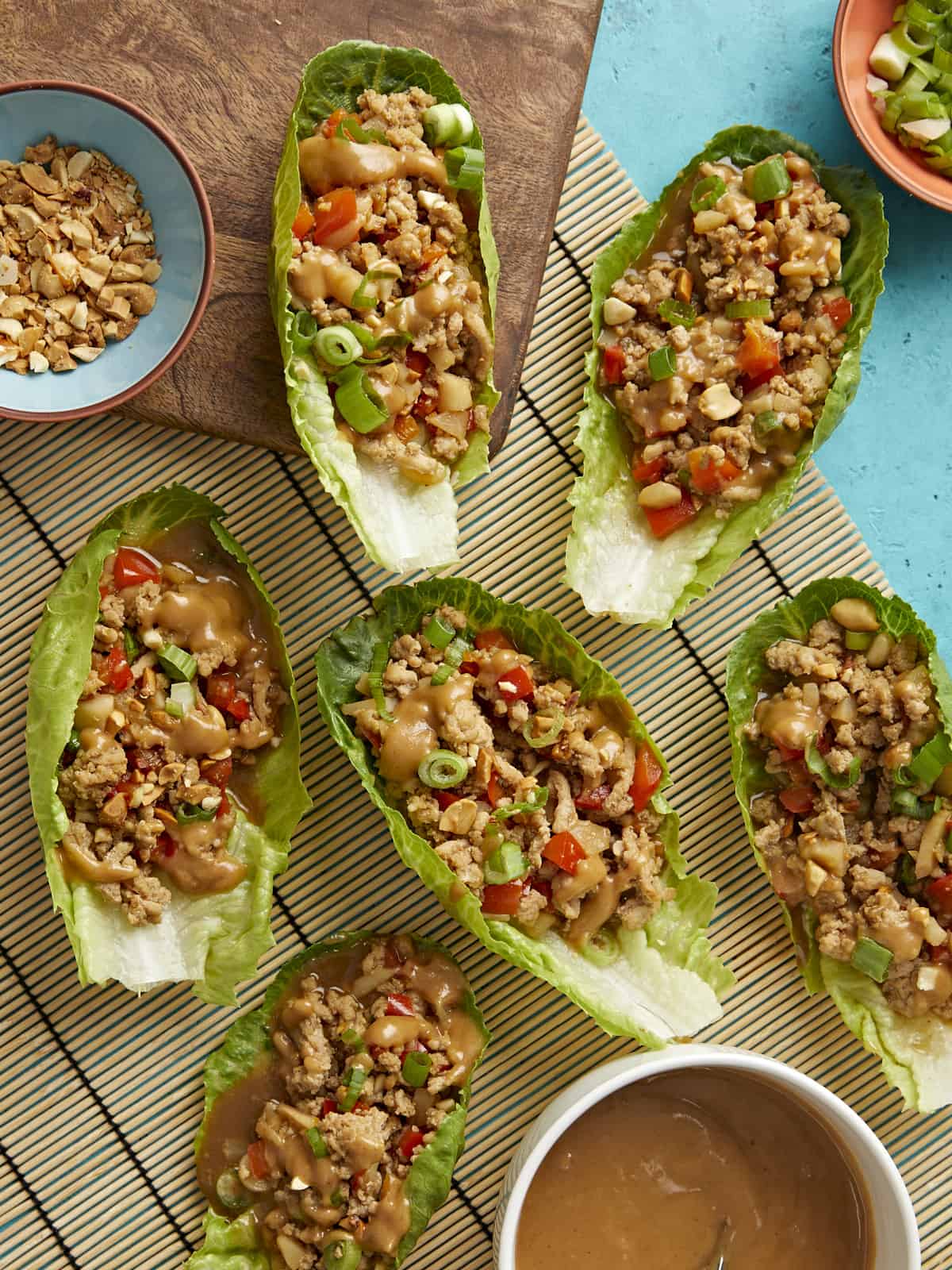 Overhead shot of chicken lettuce wraps with a small bowl of chopped peanuts and a small bowl of peanut lime dressing served on the side.