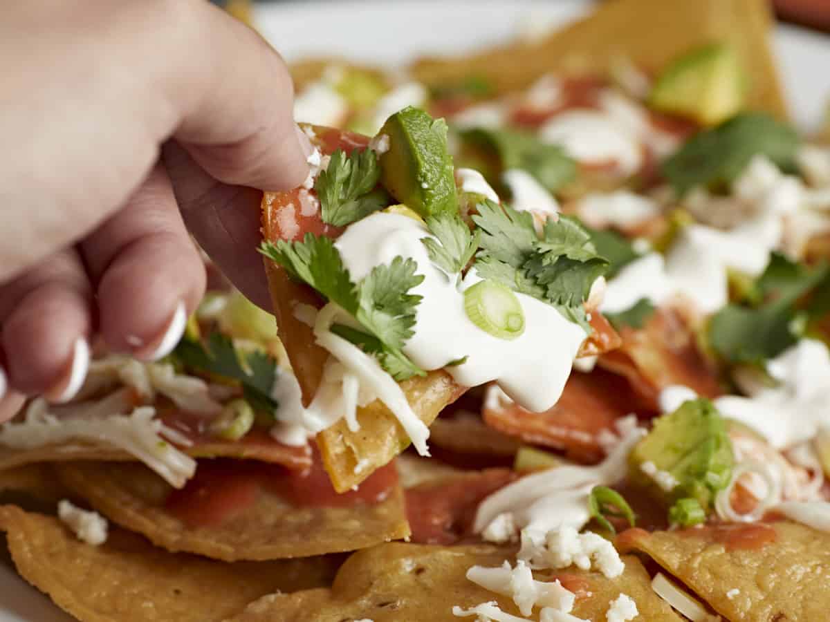 Side shot of a hand picking up a chilaquile served on a white plate.