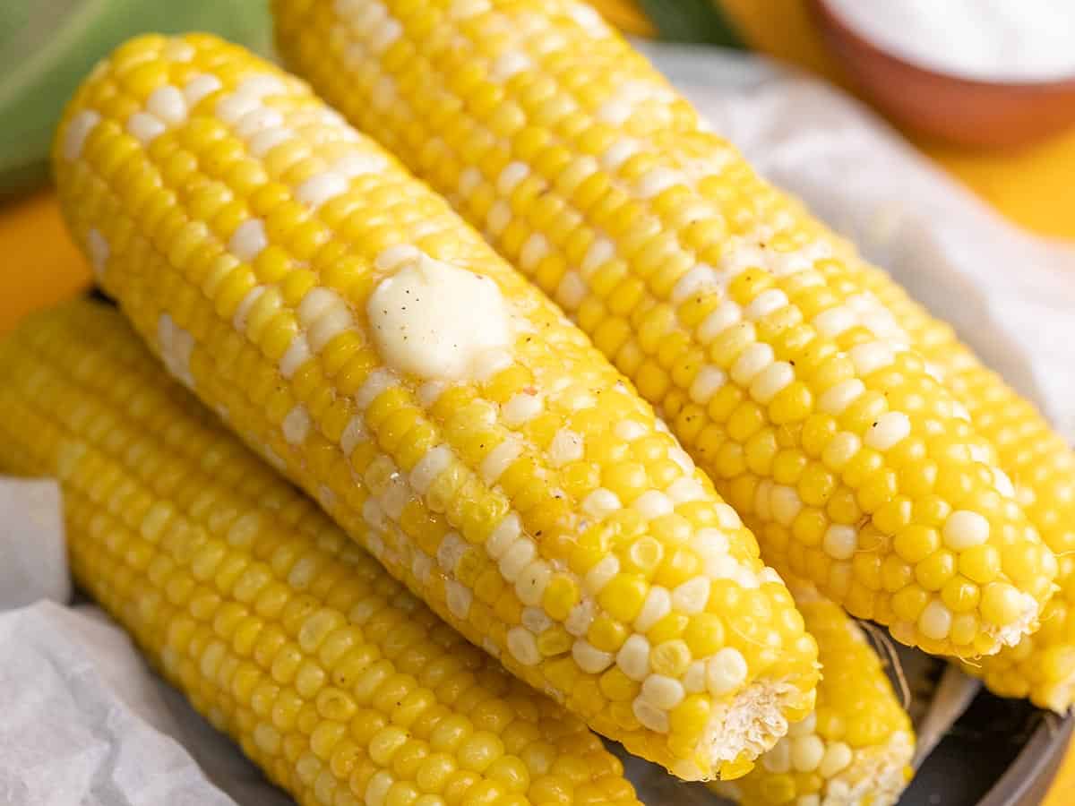 Side shot of cobs of Microwave Corn On The Cob on a black plate with a pat of butter melting on top.