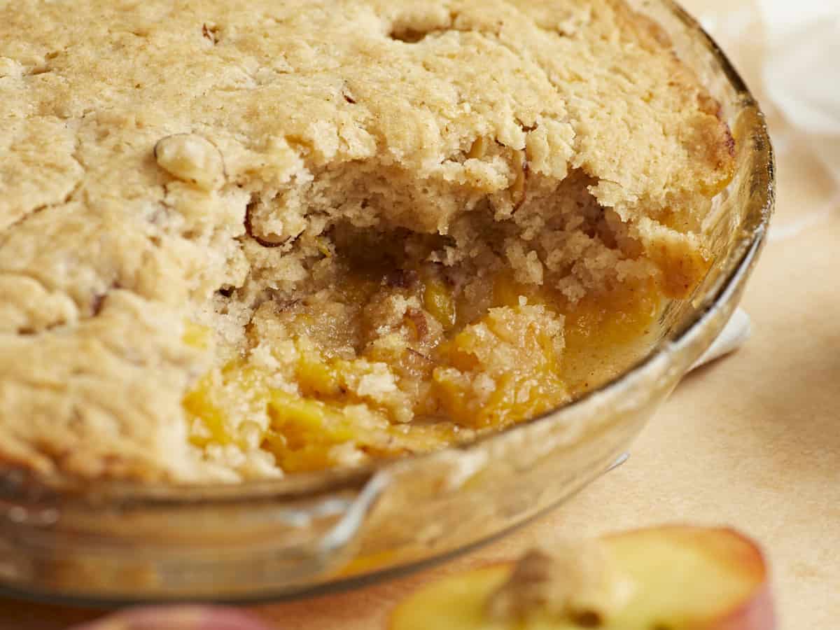 Side shot of peach cobbler with a scoop taken out in a glass pie plate.