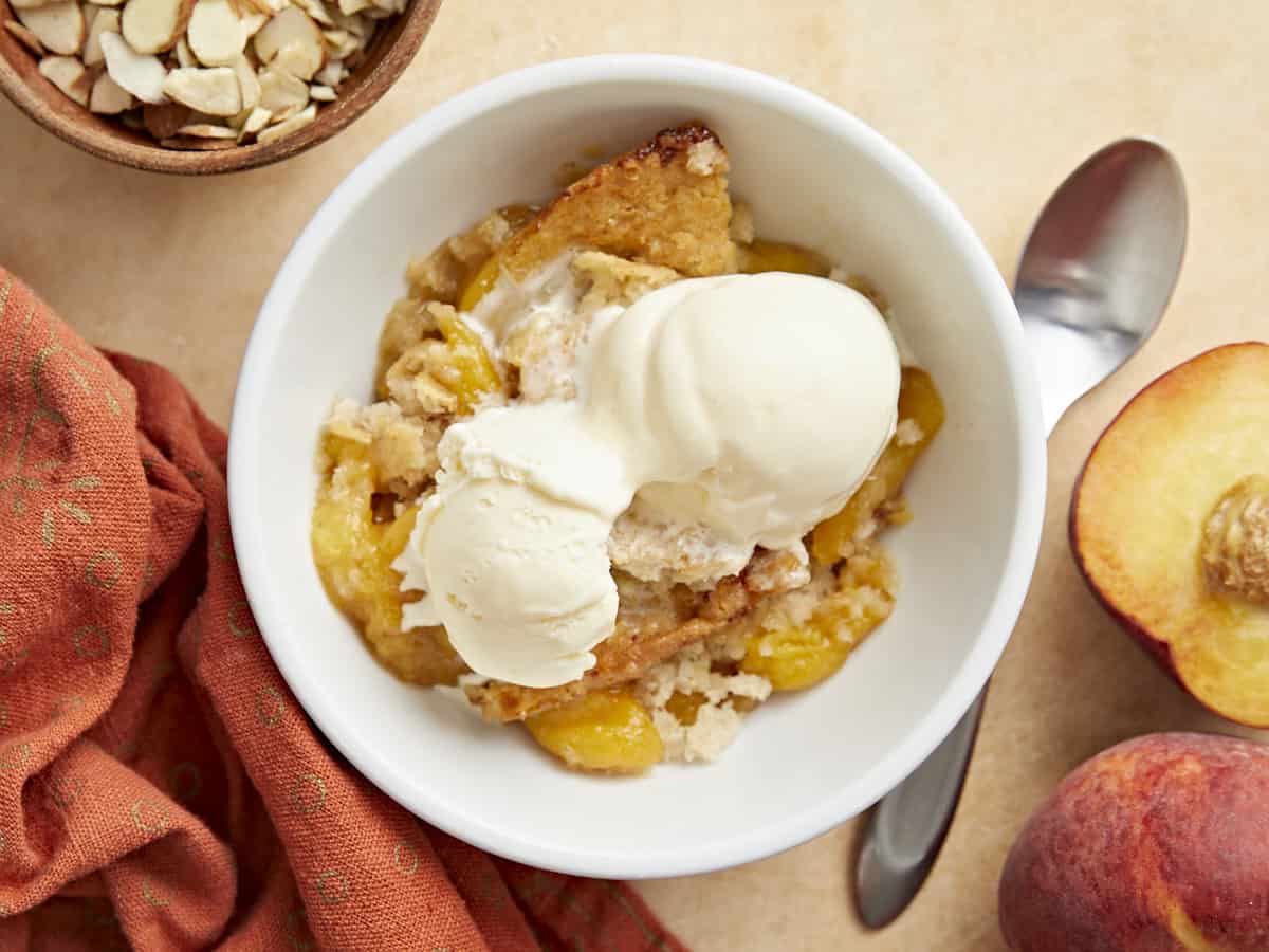 Overhead shot of a scoop of peach cobbler in a white bowl topped with a scoop of vanilla ice cream.