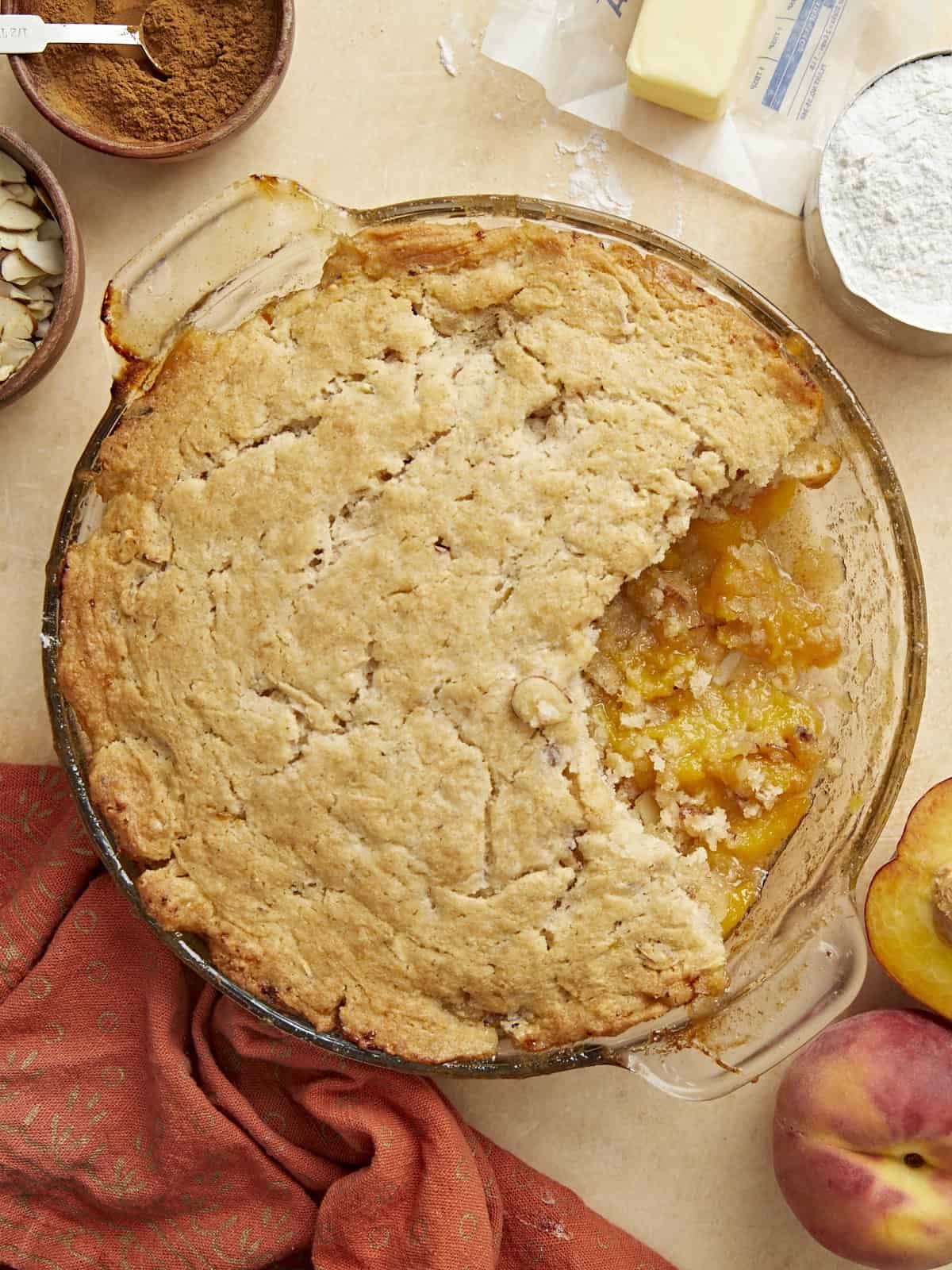 Overhead shot of peach cobbler with a scoop taken out in a glass pie plate.